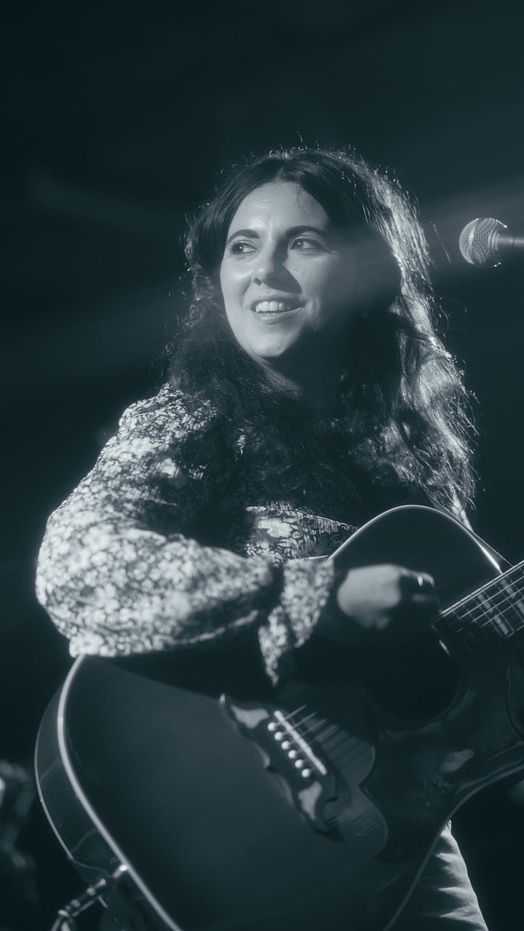 a woman holding an acoustic guitar in front of a microphone