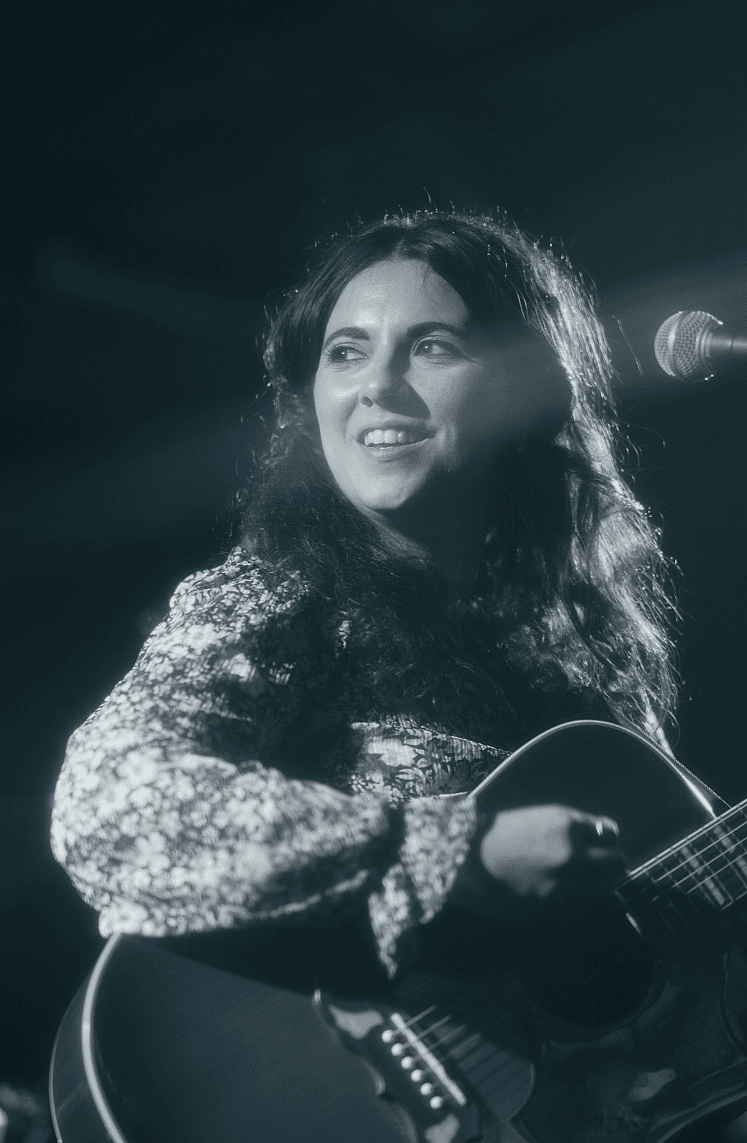 a woman playing an acoustic guitar in front of a microphone